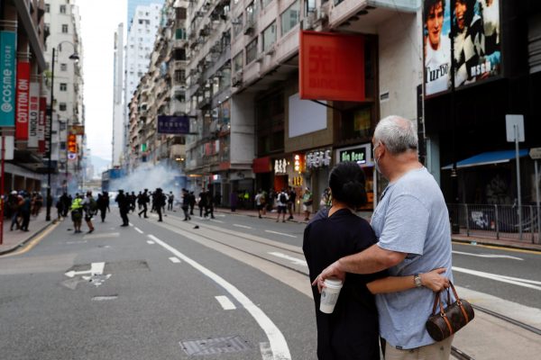 A couple hugs each other as police fire tear gas into the crowds to disperse anti-national security law protesters during a march on the anniversary of Hong Kong's handover from Britain to China, Hong Kong, 1 July 2020 (Photo: Reuters/Tyrone Siu).