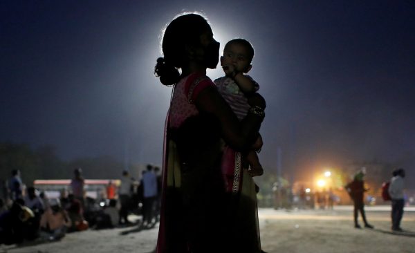 A woman and her baby wait for a bus to take them to a railway station to board a train to their home state of Uttar Pradesh, in Ghaziabad in the outskirts of New Delhi, India, 18 May 2020 (Photo: Reuters/Adnan Abidi).