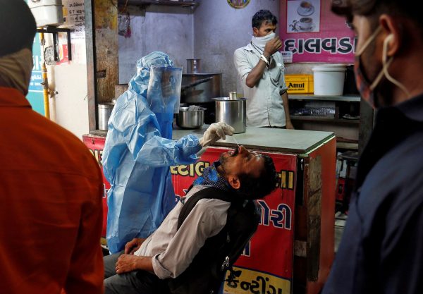 A healthcare worker wearing protective gear takes a swab sample from a man for a rapid antigen test outside a tea stall at a bus terminal in Ahmedabad, India, 15 July 2020 (Photo: Reuters/Amit Dave).