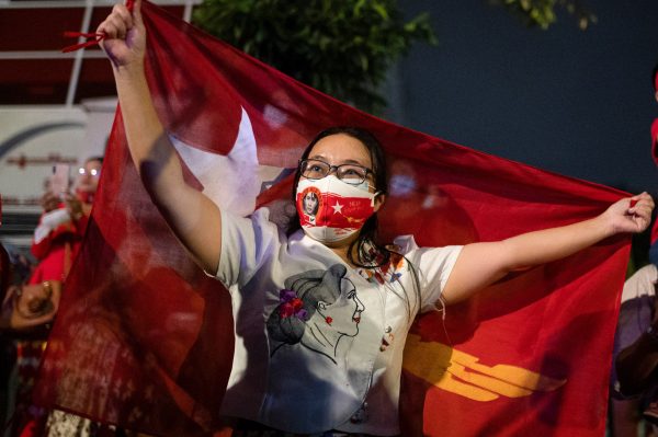 A woman holds a flag as supporters of National League for Democracy gather to celebrate at party headquarters after the general election in Yangon, Myanmar, 9 November 2020 (Photo: Reuters/Shwe Paw Mya Tin).