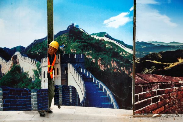 A worker looks through the fence of a construction site that is decorated with pictures of the Great Wall at Badaling, north of Beijing, China, 1 September 2016 (Photo: Reuters/Thomas Peter).