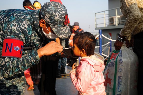 A Bangladesh navy personnel helps a child to wear a mask before getting on board a ship to move to Bhasan Char island, Bangladesh, 29 December 2020 (Photo: Reuters/Mohammad Ponir Hossain).