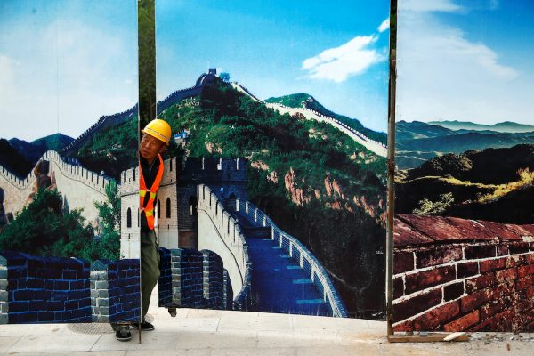 A worker looks through the fence of a construction site that is decorated with pictures of the Great Wall at Badaling, north of Beijing, China, 1 September, 2016 (Photo: Reuters/Thomas Peter).