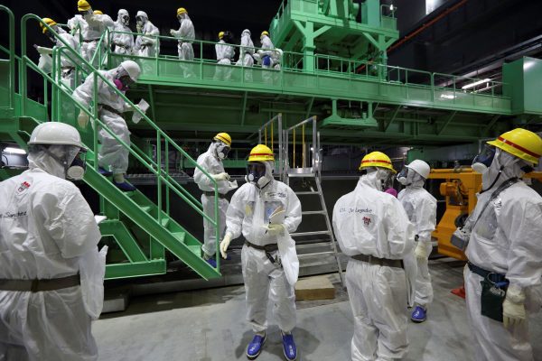 Members of the media and Tokyo Electric Power Co. (TEPCO) employees wearing protective suits and masks walk down the steps of a fuel-handling machine at the spent fuel pool inside the No.4 reactor building at the tsunami-crippled TEPCO's Fukushima Daiichi nuclear power plant in Fukushima prefecture, 7 November, 2013 (Photo: Tomohiro Ohsumi/Pool via Reuters/File Photo).