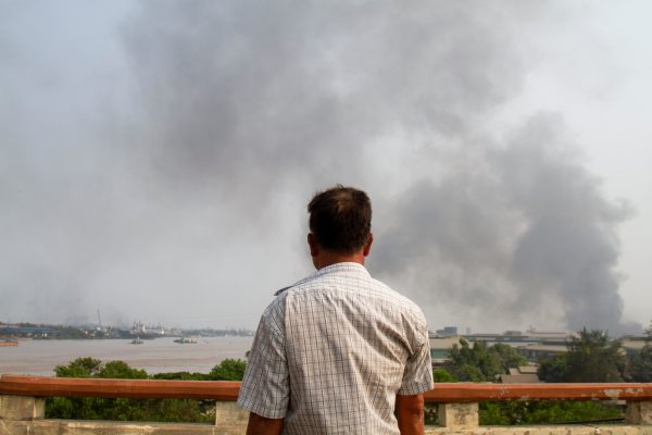 A man looks at smoke believed to be from a factory fire during the security force crackdown on anti-coup protesters at Hlaingthaya, in Yangon, Myanmar, 14 March 2021 (Photo: Reuters/Stringer).