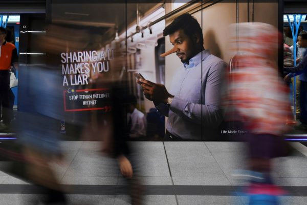 Commuters walk past an advertisement discouraging the dissemination of fake news at a train station in Kuala Lumpur, Malaysia, 28 March 2018 (Photo: Reuters/Stringer).