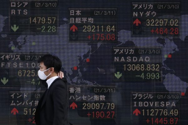 A man wearing a face mask walks past an electronic board showing currency exchange rates at a securities firm in Tokyo, March 2021 (Photo: James Matsumoto/SOPA Images/Sipa USA via Reuters)