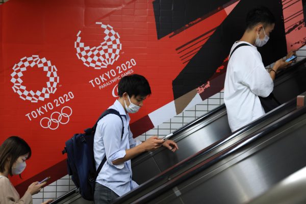 People wearing masks are seen on an escalator with Tokyo 2020 Olympic and Paralympic games branding on their background at subway station in Tokyo near the National Stadium in Shinjuku (Photo: Stanislav Kogiku/SOPA Images/Sipa USA via Reuters).
