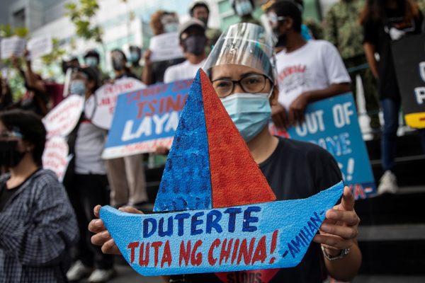 An activist holds a prop with the words 'Duterte, puppet of China' during a protest outside the Chinese Consulate in Manila's financial district, to mark the fifth anniversary of an international arbitral court ruling invalidating Beijing's historical claims over the waters of the South China Sea, in Makati City, Philippines, 12 July 2021 (Photo: Reuters/Eloisa Lopez).