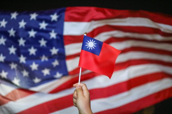 An anti-government protester holds a Taiwan national flag as a US flag flutters in the background, 10 October 2019 (Photo: Reuters/Athit Perawongmetha).