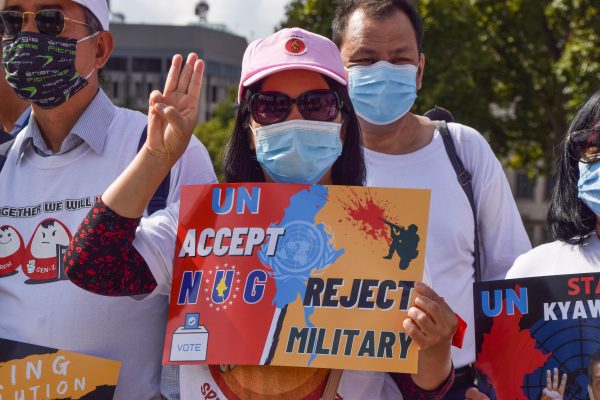 A protester holds up the three-finger salute and a placard calling on the UN to recognize the Myanmar National Unity Government and to reject the military during the demonstration in Parliament Square in London, United Kingdom (Reuters/Vuk Valcic).