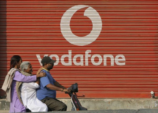 A man and two passengers ride on a scooter past a shop displaying the Vodafone logo on its shutter in Jammu, India, 21 November, 2011 (Photo: Reuters/Mukesh Gupta).