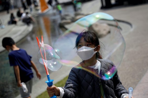 A young girl, wearing a protective mask to avoid the spread of COVID-19, plays with bubbles at a shopping mall, South Korea, 1 May, 2020 (Photo: Gimpo via Reuters).
