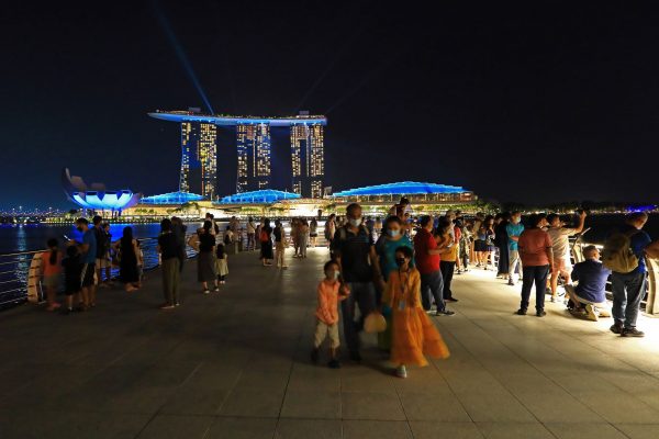 People wearing protective mask spend a night out at the Merlion Park with the Marina Bay Sands pictured in the background, Singapore, 28 December 2021 (Photo: Reuters/Suhaimi Abdullah)