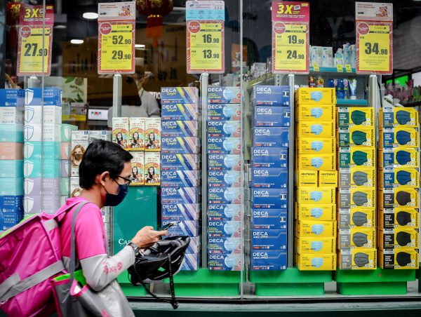 A food delivery man wearing a face mask as a preventive measure against the spread of COVID-19 walks past a pharmacy selling various face masks, 5 September 2021 (Photo: Reuters/Syaiful Redzuan).