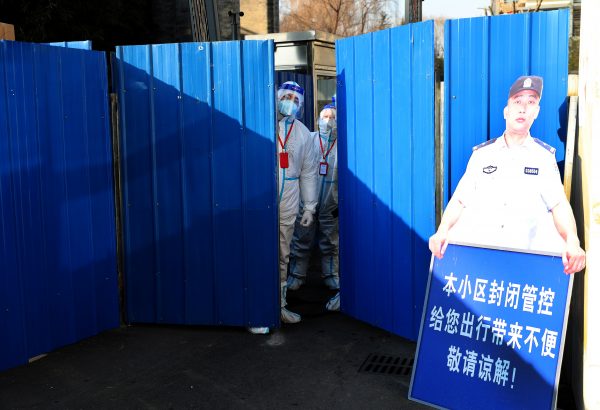 Workers wearing protective suits following the coronavirus disease (COVID-19) outbreak stand at an entrance to a residential compound under lockdown after a case of the Omicron variant was detected, in Beijing's Haidian district, China, 18 January 2022 (Photo: China Daily via Reuters).