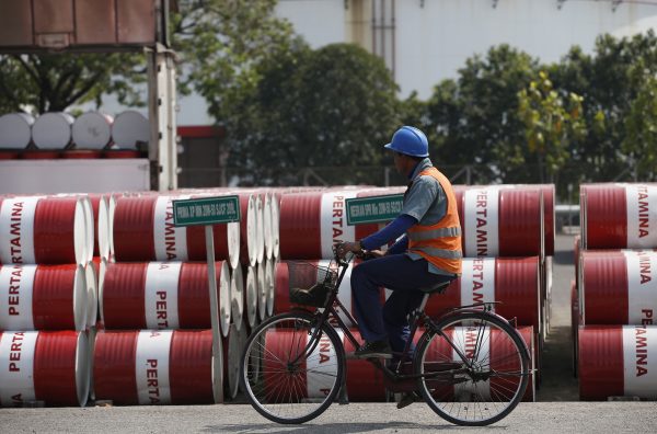 An employee rides his bike past barrels of petroleum products at a state-owned Pertamina fuel depot in Jakarta, Indonesia, 27 November 2014 (Photo: Reuters/Darren Whiteside).
