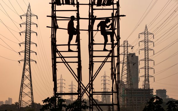 Labourers work on scaffolding set among high tension electricity pylons in Mumbai, India, October 2021 (Photo: Reuters/Francis Mascarenhas)