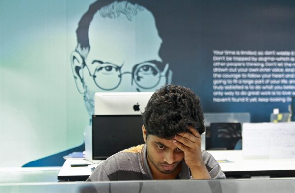 An employee works on a computer terminal against the backdrop of a picture of late Apple co-founder Steve Jobs at the Start-up Village in Kinfra High Tech Park in Kochi, India, 13 October 2012 (Photo: Reuters/Sivaram V).