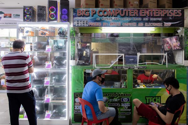 Customers wait as their devices are repaired behind a plastic barrier for protection against the coronavirus disease (COVID-19), at a computer shop in San Juan City, Metro Manila, Philippines 23 July 2020 (REUTERS/Eloisa Lopez).