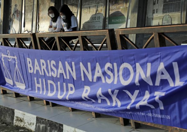Nur Fadzlina Dahlan, 23, (left) and Nur Izzati Fitrah, 23, stand at a bus stop decorated with a Barisan Nasional banner, during the campaign period of Johor state election at Johor Baru, Johor, Malaysia, 4 March 2022. (Photo: Reuters/Hasnoor Hussain)