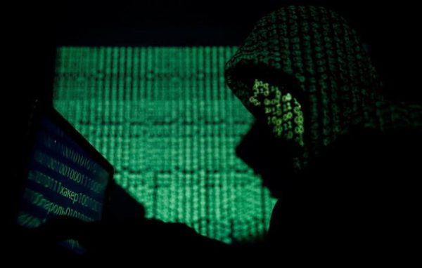 A hooded man holds a laptop computer as cyber code is projected on him (Photo: Reuters/Kacper Pempel).