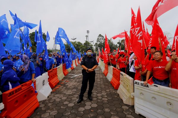 A police stands guard between supporters of The National Front coalition, Barisan Nasional, and The Alliance Of Hope, Pakatan Harapan, outside a nomination centre on nomination day in Bera, Pahang, Malaysia, 5 November 2022 (Photo: Reuters/Lai Seng Sin).