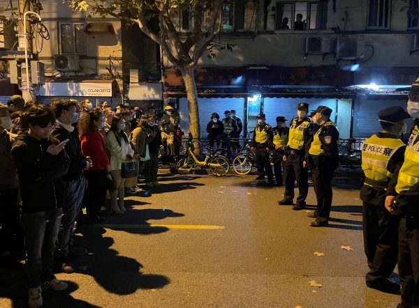 People stand in front of a line of police officers during a demonstration against COVID-19 curbs in Shanghai, China, 27 November 2022. (PHOTO: Casey Hall via REUTERS)
