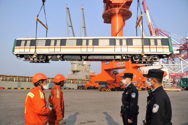 Police officers and dock workers wearing face masks to prevent the spread of COVID-19 stand near a railway carriage to be shipped to Singapore, at a port in Qingdao, Shandong province, China, 18 March 2020 (Photo: China Daily/Reuters).