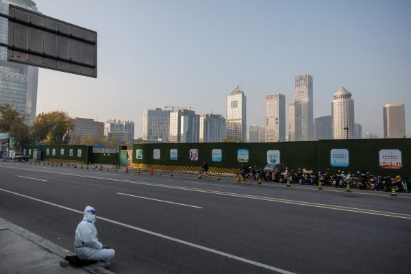 An epidemic prevention worker in a protective suit sits on the pavement in the Central Business District (CBD) as outbreaks of the coronavirus disease (COVID-19) continue in Beijing, China, 23 November 2022. (Photo: Reuters/Thomas Peter)