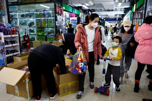 A woman and a child walk past workers sorting toys at a shopping mall in Beijing, China, 11 January 2023 (Photo: Reuters/Tingshu Wang).