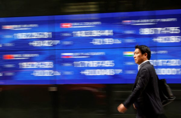 A passerby walks past an electric monitor displaying various countries' stock price index outside a bank in Tokyo, Japan, 22 March 2023 (Photo: Reuters/Issei Kato).