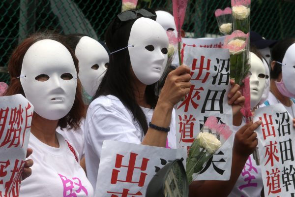 Masked Taiwanese human rights activists hold banners saying 
