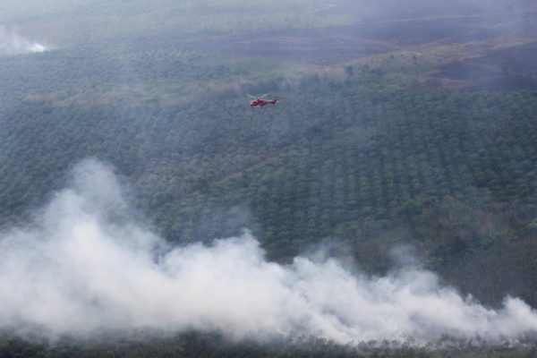 A helicopter carrying a water bucket is seen after dropping water on palm oil plantation in Ogan Komering Ilir, Indonesia, 18 July, 2018 (Photo: Reuters/Nova Wahyudi).