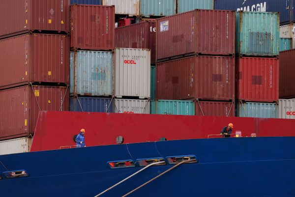 Workers are seen in front of shipping containers stacked on a container ship docked inside Botany Bay, Sydney, Australia, 28 October 2020 (Photo: Reuters/Loren Elliott).