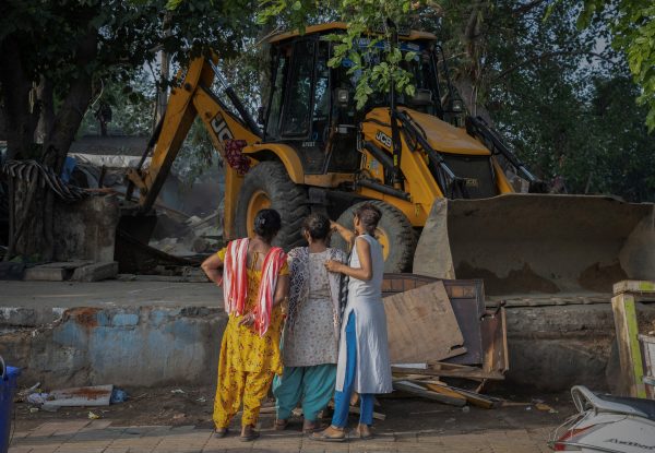 Women watch as an excavator detroys their houses during a demolition drive by the authorities at a slum area next to the G20 Summit main venue in New Delhi, India, 1 June 2023 (Photo: Reuters/Adnan Abidi).