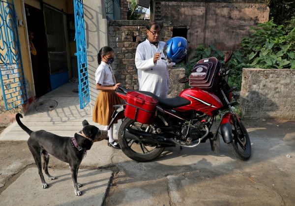 Ambika Chatterjee, 9, a fifth-grade student, who according to her father Subhasish Chatterjee, 52, shifted to a low fee charging private school from an elite school, waits for her father as he puts on his helmet to drop her to a school in Kolkata, India, 27 April 2022 (Photo: Reuters/Rupak De Chowdhuri).
