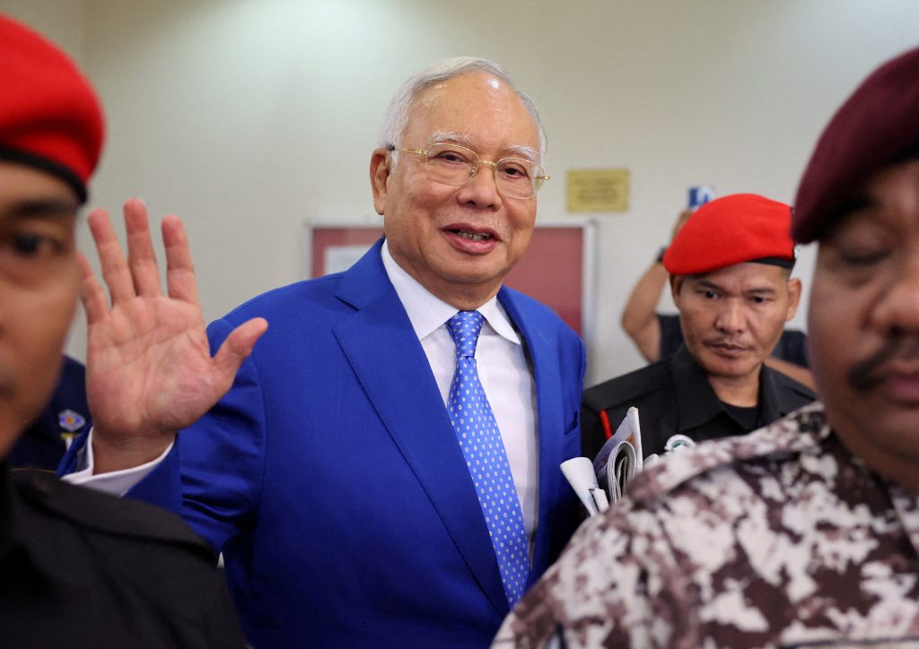 Former Malaysian Prime Minister Najib Razak escorted by prison officers, waves to photographers as the jailed politician leaves the court after court proceedings in Kuala Lumpur, Malaysia, 19 January 2024 (Photo: Reuters/Hasnoor Hussain).