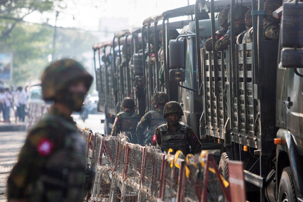 Soldiers stand next to military vehicles as people gather to protest against the military coup in Yangon, Myanmar, 15 February 2021 (Photo: Reuters).