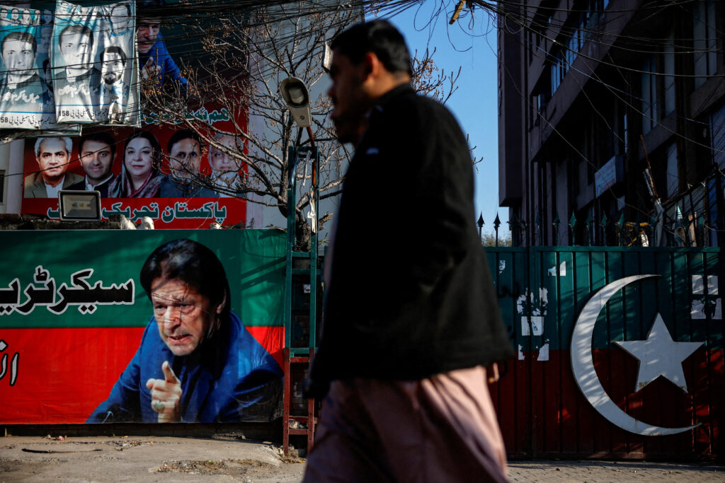 People walk past a banner with a picture of the former Prime Minister Imran Khan outside the party office of Pakistan Tehreek-e-Insaf (PTI), a day after the general election, in Lahore, Pakistan, 9 February 2024 (Photo: Reuters/Navesh Chitrakar).
