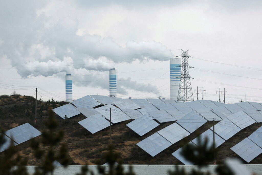 Smoke rises from chimneys near solar panels, during a Huawei-organised media tour, in Shaanxi province, China, 24 April 2023 (Photo: Reuters/Tingshu Wang).